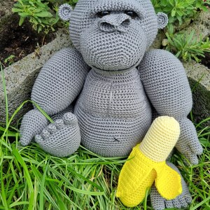 May include: A grey crocheted gorilla toy sitting in green grass with a yellow crocheted banana toy.