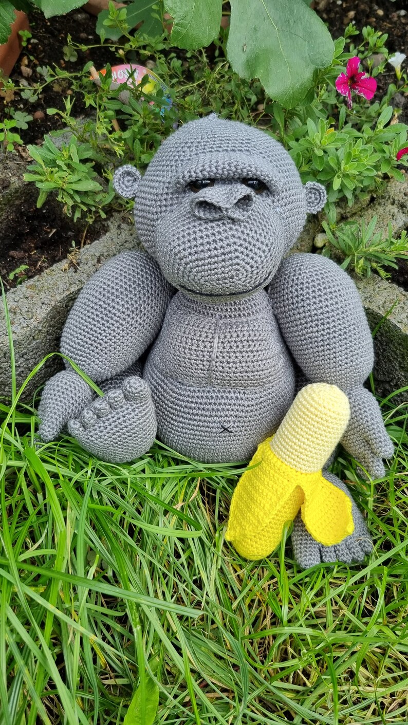 May include: A grey crocheted gorilla toy sitting in green grass with a yellow crocheted banana toy.