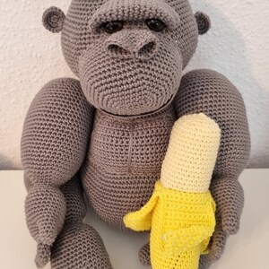 May include: A grey crocheted gorilla toy holding a yellow crocheted banana.