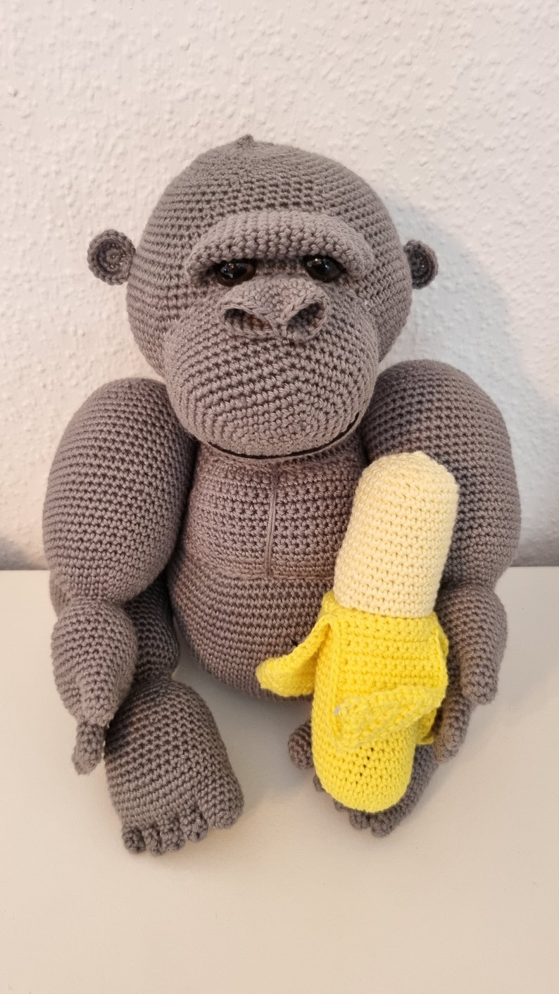 May include: A grey crocheted gorilla toy holding a yellow crocheted banana.