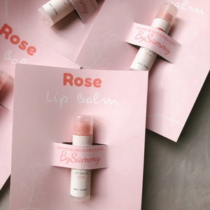 May include: Three pink and white labels with the text "Rose Lip Balm" and "Homemade & Organic By Sammy" on them. Each label has a small tube of lip balm with a pink and white label that says "Lip Balm Rose" and "Homemade & Organic By Sammy".