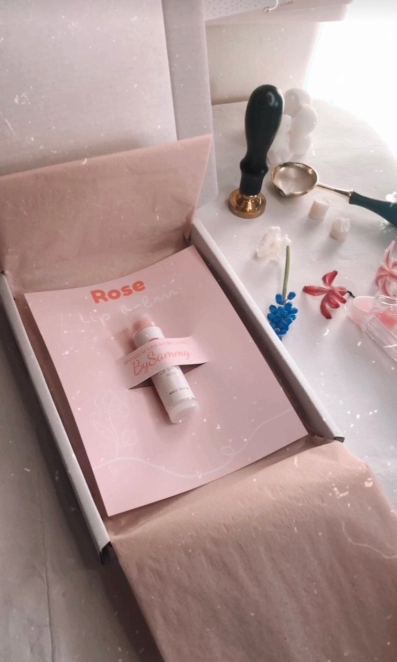 May include: A pink and white box with a pink and white card that says "Rose Lip Balm" and a white tube of lip balm that says "Gimme that moisture" and "By Sammy".