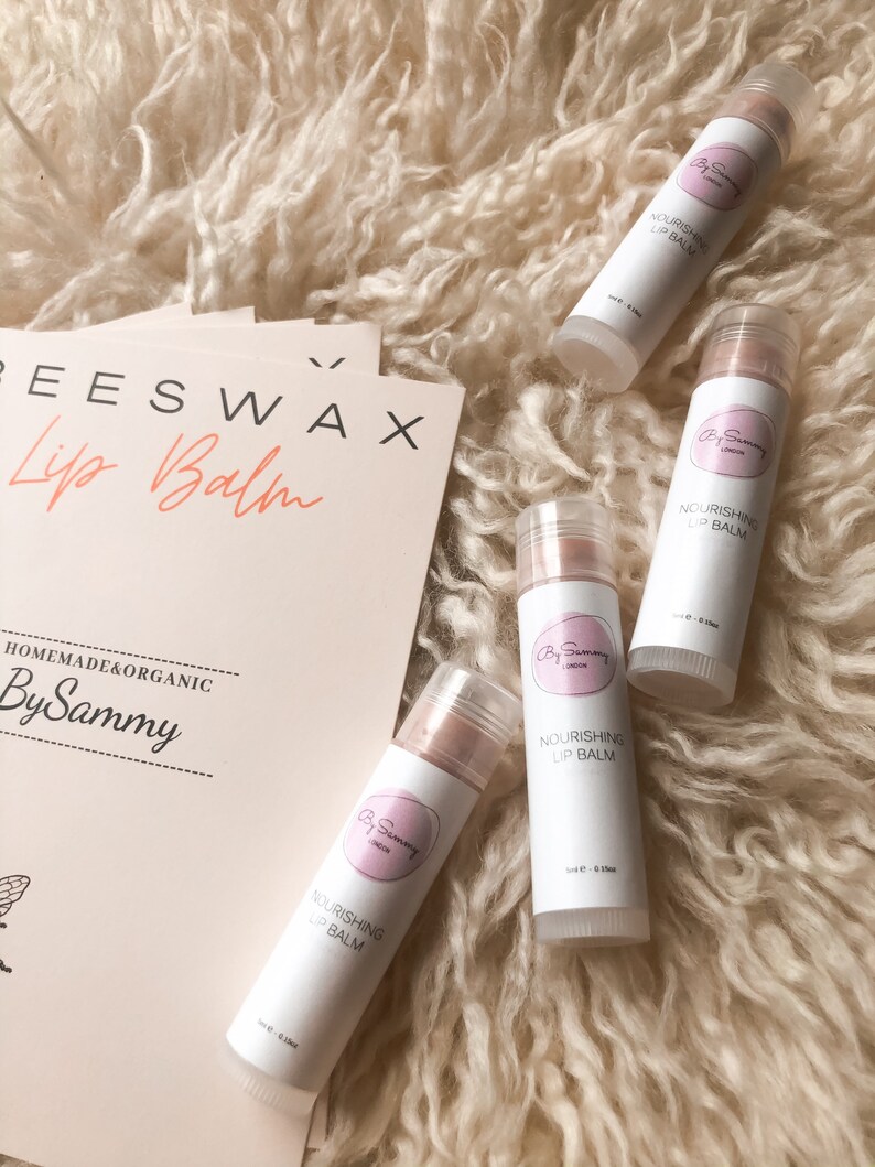 Op de afbeelding: Vier witte tubes lippenbalsem met roze etiketten. De etiketten zeggen "Nourishing Lip Balm" en "By Sammy London".