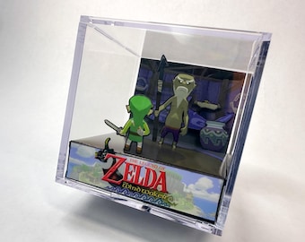 Puede incluir: Una vitrina de acrílico transparente con una escena de "The Legend of Zelda: Wind Waker". El diorama incluye recortes de personajes de Link y un anciano, sobre un fondo pintado. El logotipo del juego es visible.