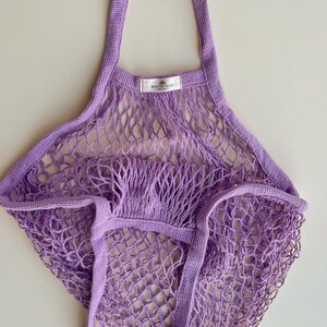 May include: A lavender string mesh bag with a label that reads "SUN & CHILD STUDIO".