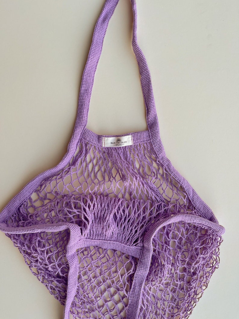 May include: A lavender string mesh bag with a label that reads "SUN & CHILD STUDIO".