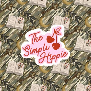 May include: A repeating pattern featuring open books with floral illustrations, antique keys, crescent moons, and leafy branches on a camouflage-style background. A pink sticker with the text "The Simple Hippie" and cherry graphics is in the center.