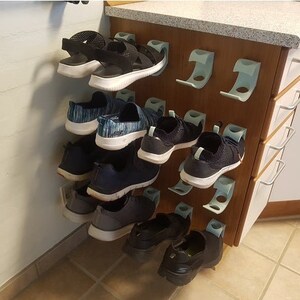 May include: A wall-mounted shoe rack with a light wood finish and white plastic shoe holders. The rack is filled with a variety of shoes, including sandals, sneakers, and flats.