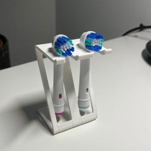May include: White plastic toothbrush head holder with two toothbrush heads. One head is blue and green, the other is pink and blue.