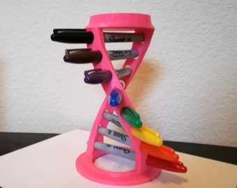 May include: A pink 3D printed pen holder shaped like a double helix. The holder has slots for pens and markers. The holder is filled with a variety of colored markers.