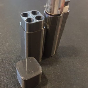 May include: A black plastic container with four round holes in the top, a black plastic lid, and a black lighter with a silver top.