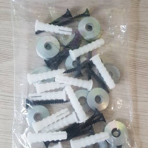 May include: A clear plastic bag filled with white plastic anchors, black screws, and silver metal washers. These are common hardware items used for hanging pictures or other objects on walls.