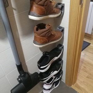 May include: A set of four shoes organized on a wall-mounted shoe rack. The rack is made of gray plastic and has a simple design. The shoes include two pairs of brown leather boots and two pairs of black and white sneakers.