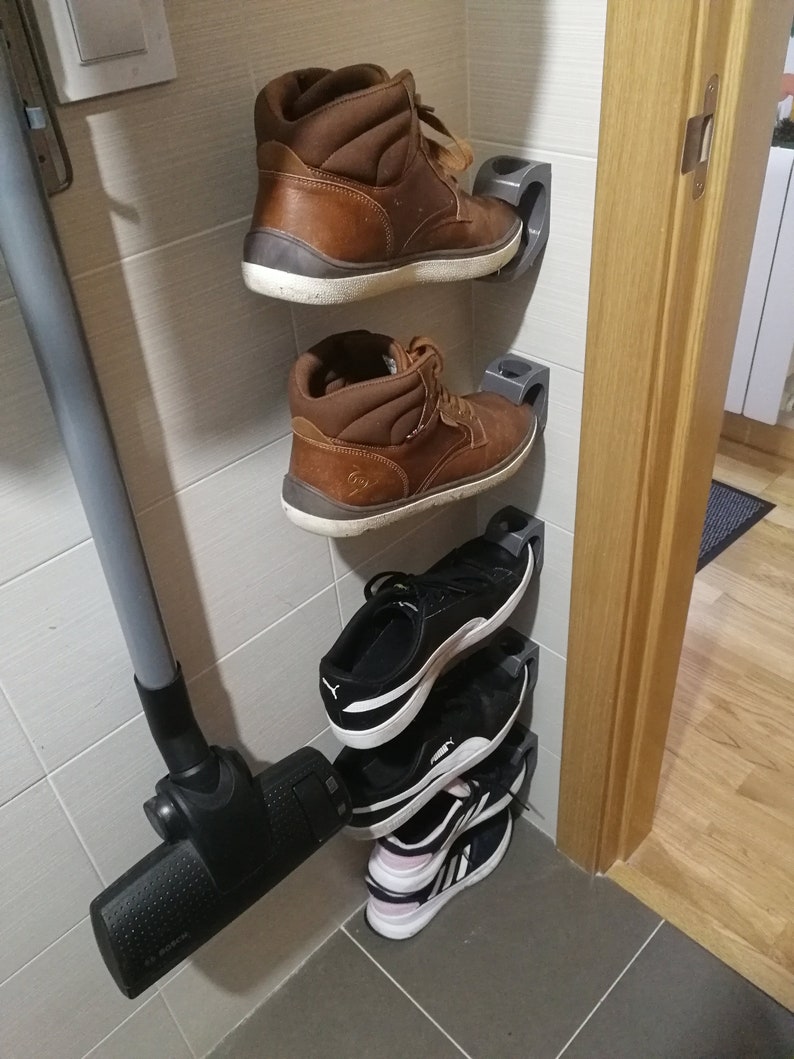 May include: A set of four shoes organized on a wall-mounted shoe rack. The rack is made of gray plastic and has a simple design. The shoes include two pairs of brown leather boots and two pairs of black and white sneakers.