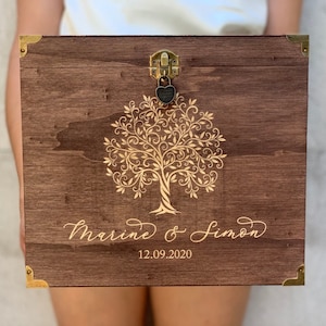 May include: A wooden box with a gold tree design and the text "Marine & Simon 12.09.2020" engraved on the front. The box has a brass lock and hinge.