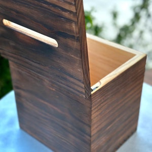 May include: A handcrafted wooden box with a hinged lid and a rectangular handle cutout. The box is made of dark stained wood, showcasing the natural grain. The interior is a lighter wood color.