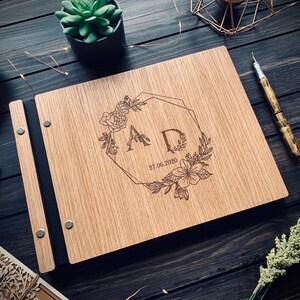 May include: A wooden guest book with a black leather binding. The cover is engraved with a floral design, the initials "AD", and the date "27.06.2020".