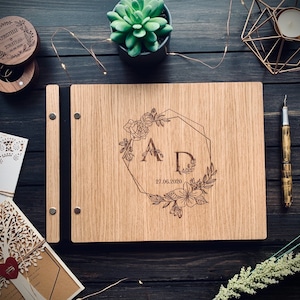 May include: A wooden guest book with a floral design and the initials "A D" engraved on the front. The date "27.06.2020" is also engraved on the book.