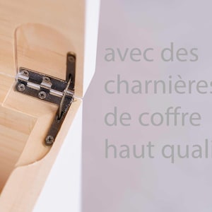 May include: Close-up of a wooden box hinge with a metal hinge and screws. The box is light-colored wood, and the hinge is a dark metal. Text in the background reads "avec des charni&egrave;res de coffre haut qualit&eacute;."