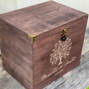 K&ouml;nnte beinhalten: Eine Holzkiste mit einem Schlitz oben und einem Schloss mit Schl&uuml;ssel. Die Kiste ist mit einem Baummotiv und dem Text "Marriage of Jared 12.09.2020" verziert.