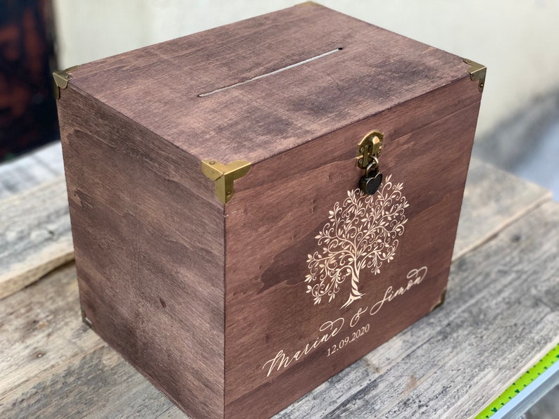 K&ouml;nnte beinhalten: Eine Holzkiste mit einem Schlitz oben und einem Schloss mit Schl&uuml;ssel. Die Kiste ist mit einem Baummotiv und dem Text "Marriage of Jared 12.09.2020" verziert.