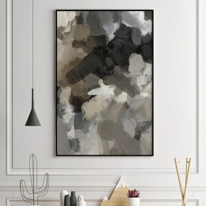 May include: A black framed abstract painting with shades of brown, gray, and white. The painting is hanging on a white wall above a wooden desk with a cactus, plants, and decorative items.