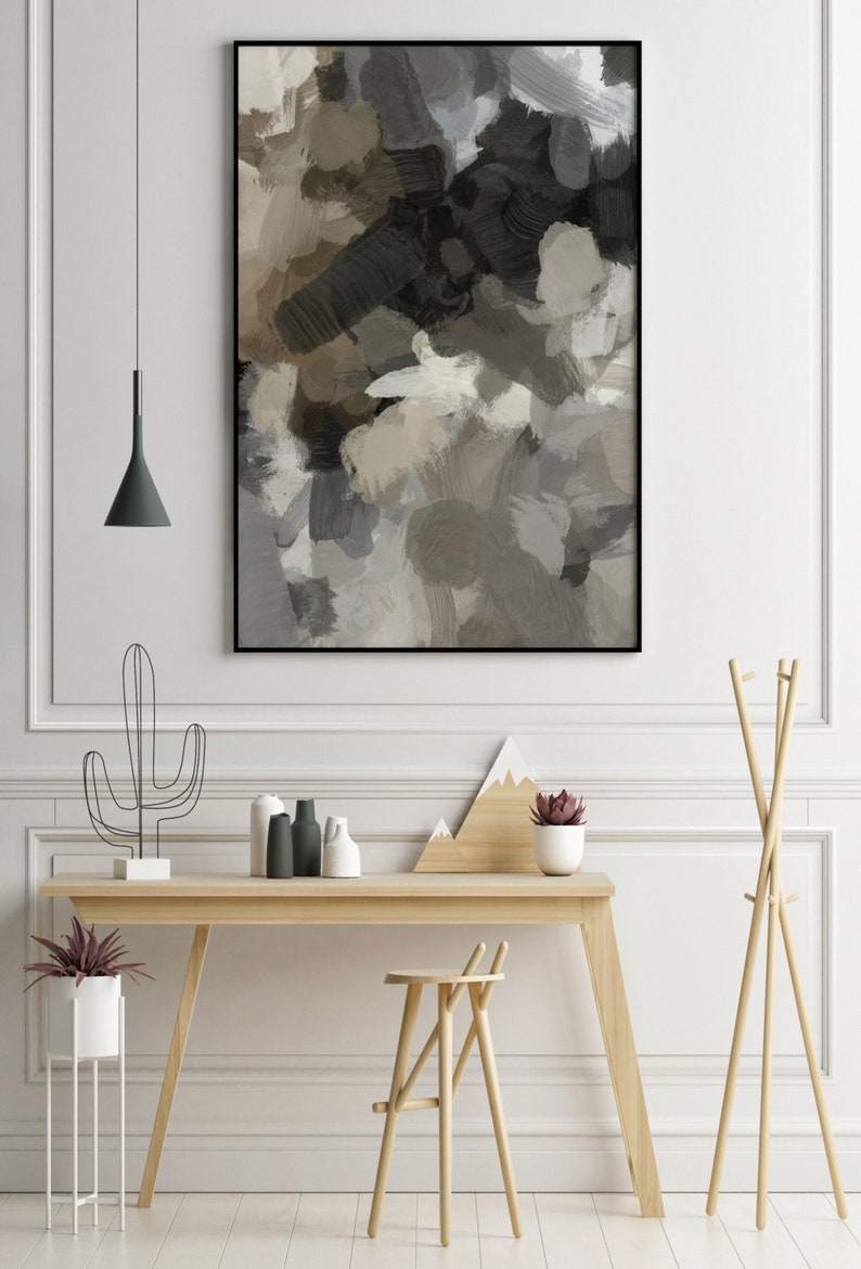 May include: A black framed abstract painting with shades of brown, gray, and white. The painting is hanging on a white wall above a wooden desk with a cactus, plants, and decorative items.