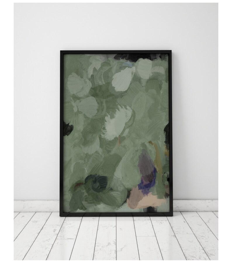 May include: Abstract art print in a black frame. The artwork features a blend of green, white, and black brushstrokes, creating a textured, painterly effect. The piece is displayed against a white wall and a white wooden floor.