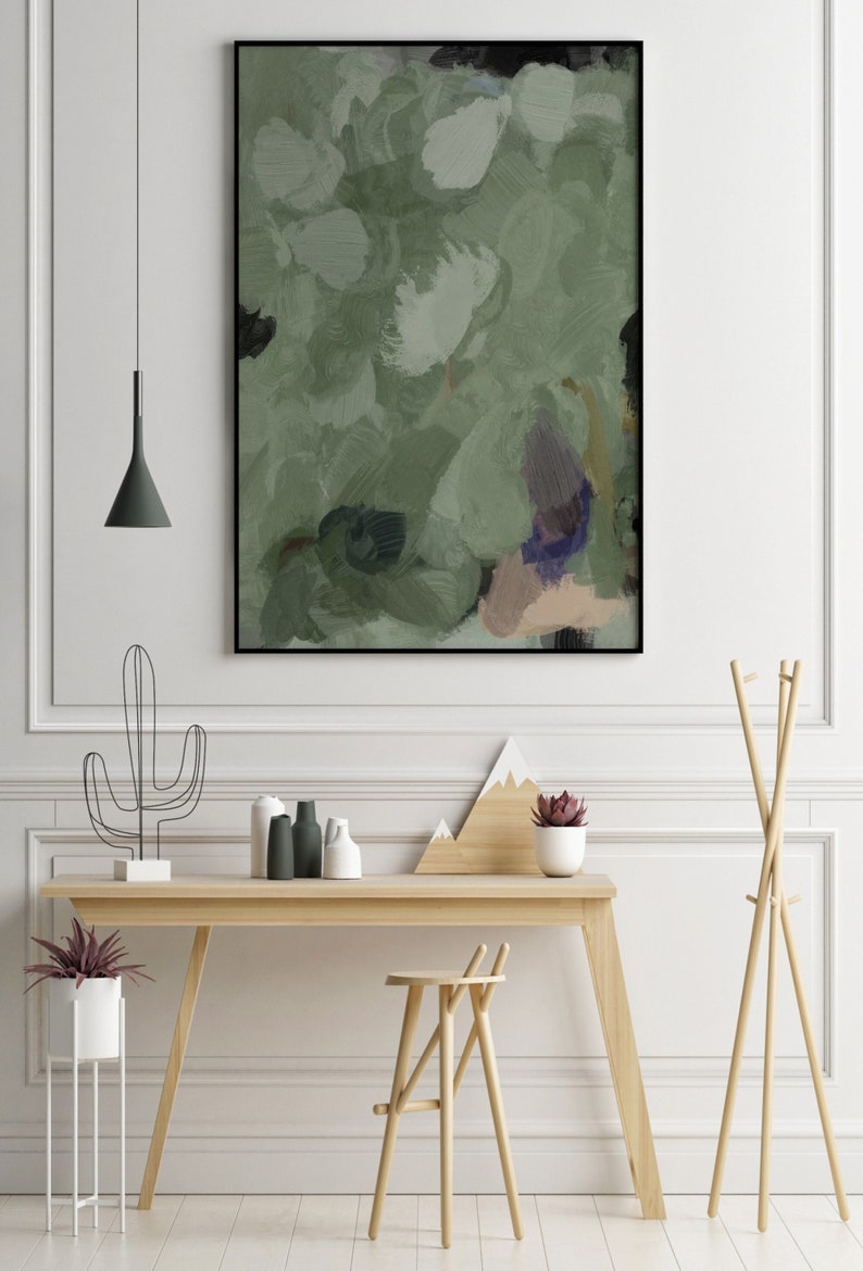 May include: Abstract art print in a black frame. The artwork features a blend of green, white, and neutral tones, with visible brushstrokes. The painting is displayed above a wooden desk with decorative items, including a cactus sculpture and vases.