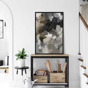 May include: A black framed abstract painting with brown, gray, and white brushstrokes hangs above a black metal console table with two wooden storage boxes. The table has a wooden top and wheels.