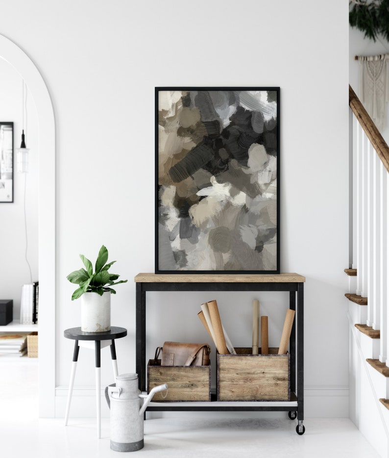 May include: A black framed abstract painting with brown, gray, and white brushstrokes hangs above a black metal console table with two wooden storage boxes. The table has a wooden top and wheels.