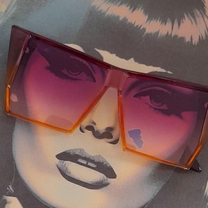 May include: Oversized square sunglasses with a gradient lens, transitioning from purple to orange. The frames are a translucent orange color. The sunglasses are placed over a black and white illustration of a face.