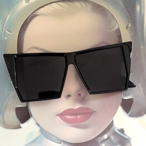 May include: A woman wearing black, angular sunglasses with a thick frame. The sunglasses have a dark lens and a sharp, geometric shape.