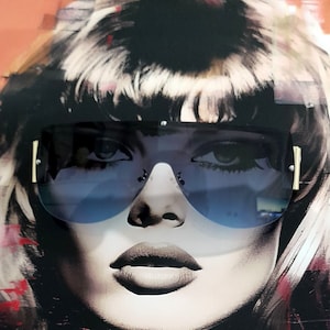 May include: A woman with short, dark hair is wearing large, blue-tinted sunglasses with a black frame. The background is a colorful abstract design.