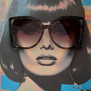 May include: Large, square-framed sunglasses with a tortoiseshell pattern. The sunglasses have dark lenses and are set against a pop art style image of a woman's face. The overall aesthetic is retro and stylish.