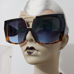 Könnte beinhalten: Überdimensionale Sonnenbrille in Schwarz und braunem Schildpatt mit einem goldenen Metallbügel über der Brücke.