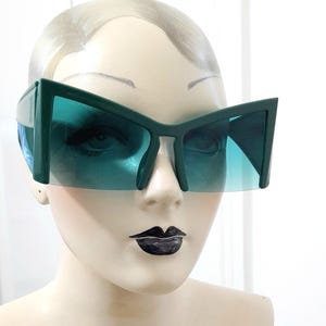 May include: A set of three ceramic mugs with a speckled, cream-colored glaze. Each mug features a different hand-painted design: a blue and green leaf, a yellow flower, and a red berry. The mugs have a simple, rounded shape.