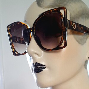 May include: Large, square-framed sunglasses with a tortoiseshell pattern. The lenses are dark, providing shade. The sunglasses are on a mannequin head, showcasing the eyewear's design and style.