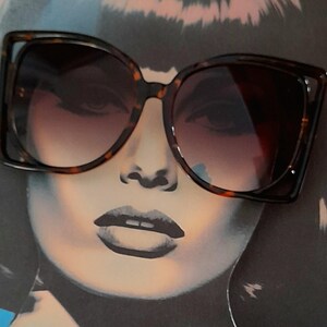 May include: Large, square-framed sunglasses with a tortoiseshell pattern. The lenses have a gradient tint, transitioning from dark at the top to lighter at the bottom. The sunglasses are set against a backdrop of a stylized face.
