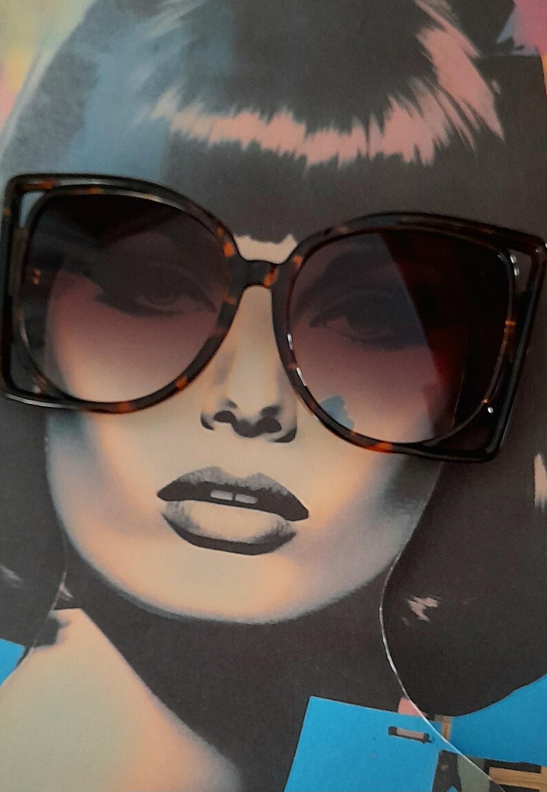 May include: Large, square-framed sunglasses with a tortoiseshell pattern. The lenses have a gradient tint, transitioning from dark at the top to lighter at the bottom. The sunglasses are set against a backdrop of a stylized face.