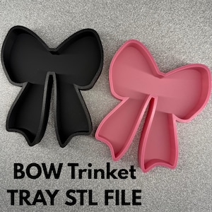 May include: Two bow-shaped trinket trays, one black and one pink, are shown on a textured silver surface. The text "BOW Trinket TRAY STL FILE" is printed in white below the trays. These trays are designed to hold small items.