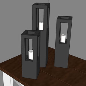 May include: Three black metal candle holders with square bases and open frames. Each holder has a white candle inside.
