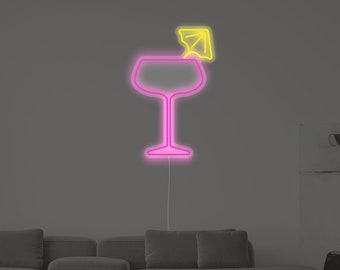 May include: A pink neon sign of a cocktail glass with a yellow neon umbrella on top. The sign is mounted on a wall above a gray couch.