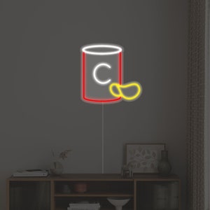 May include: A neon sign depicting a red can with a white outline and the letter "C" inside. A yellow neon shape resembling a chip is next to the can.