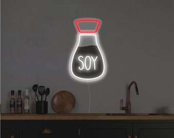 May include: A neon sign in the shape of a soy sauce bottle, with the word "SOY" in white. The sign has a white outline and a red cap. It is mounted on a white brick wall above a black kitchen cabinet.
