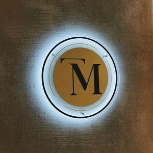 May include: A gold circle with a black "TM" logo inside, illuminated by a white halo.