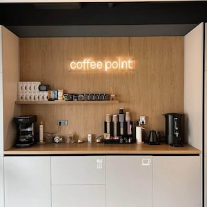 Puede incluir: Un punto de café con un letrero de neón, una cafetera y una variedad de suministros para el café.