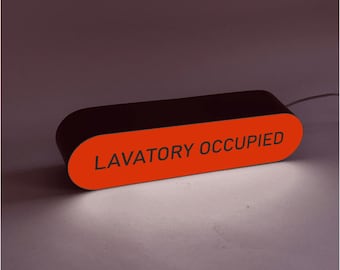 May include: An oblong, horizontal sign with a black frame and a bright orange front panel. The text LAVATORY OCCUPIED is printed in black, sans-serif capital letters across the center. The sign emits a soft white light from its base.