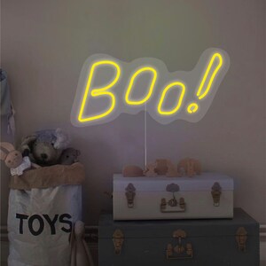 May include: A yellow neon sign that says "BOO!" is displayed above a stack of two vintage trunks. A canvas bag labeled "TOYS" is filled with stuffed animals. The scene is set in a child's room.