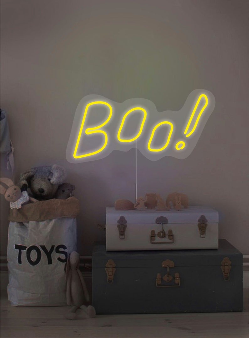 May include: A yellow neon sign that says "BOO!" is displayed above a stack of two vintage trunks. A canvas bag labeled "TOYS" is filled with stuffed animals. The scene is set in a child's room.